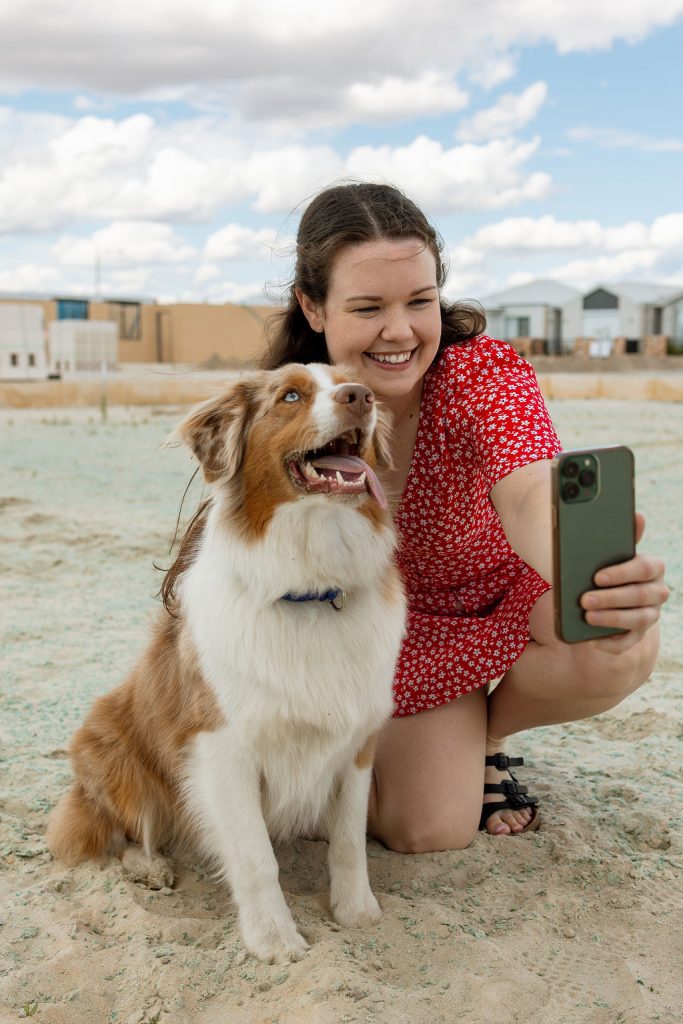 Smiling first home buyer taking a selfie with her dog outside a new home